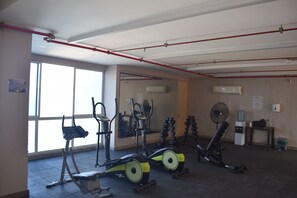 Ein Fitnessstudio mit verschiedenen Trainingsgeräten, darunter ein Fahrradergometer, ein Crosstrainer und Kurzhanteln.