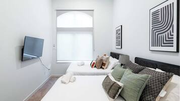 Un dormitorio moderno con un ventanal grande, un televisor de pantalla plana en la pared y dos camas con varios almohadones y una mesita de noche.