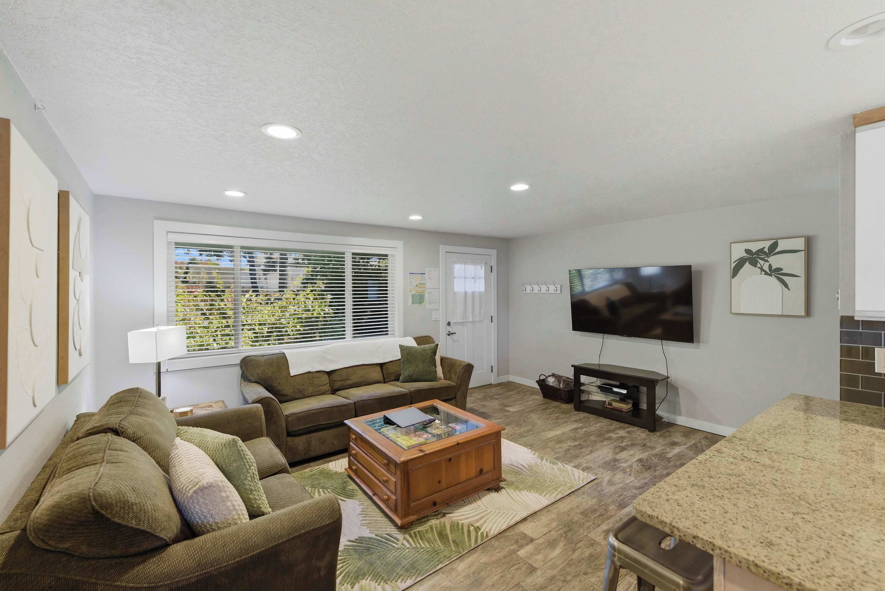A living room with a sofa, coffee table, TV, and a window with blinds.