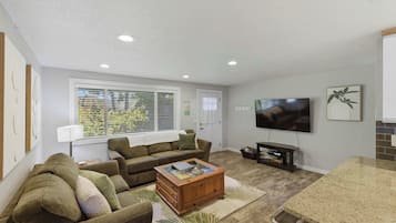 A living room with a sofa, coffee table, TV, and a window with blinds.