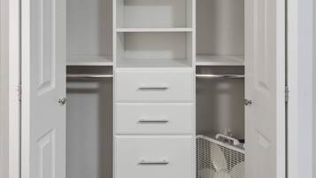 A walk-in closet with white shelving, a folding chair, and a fan.