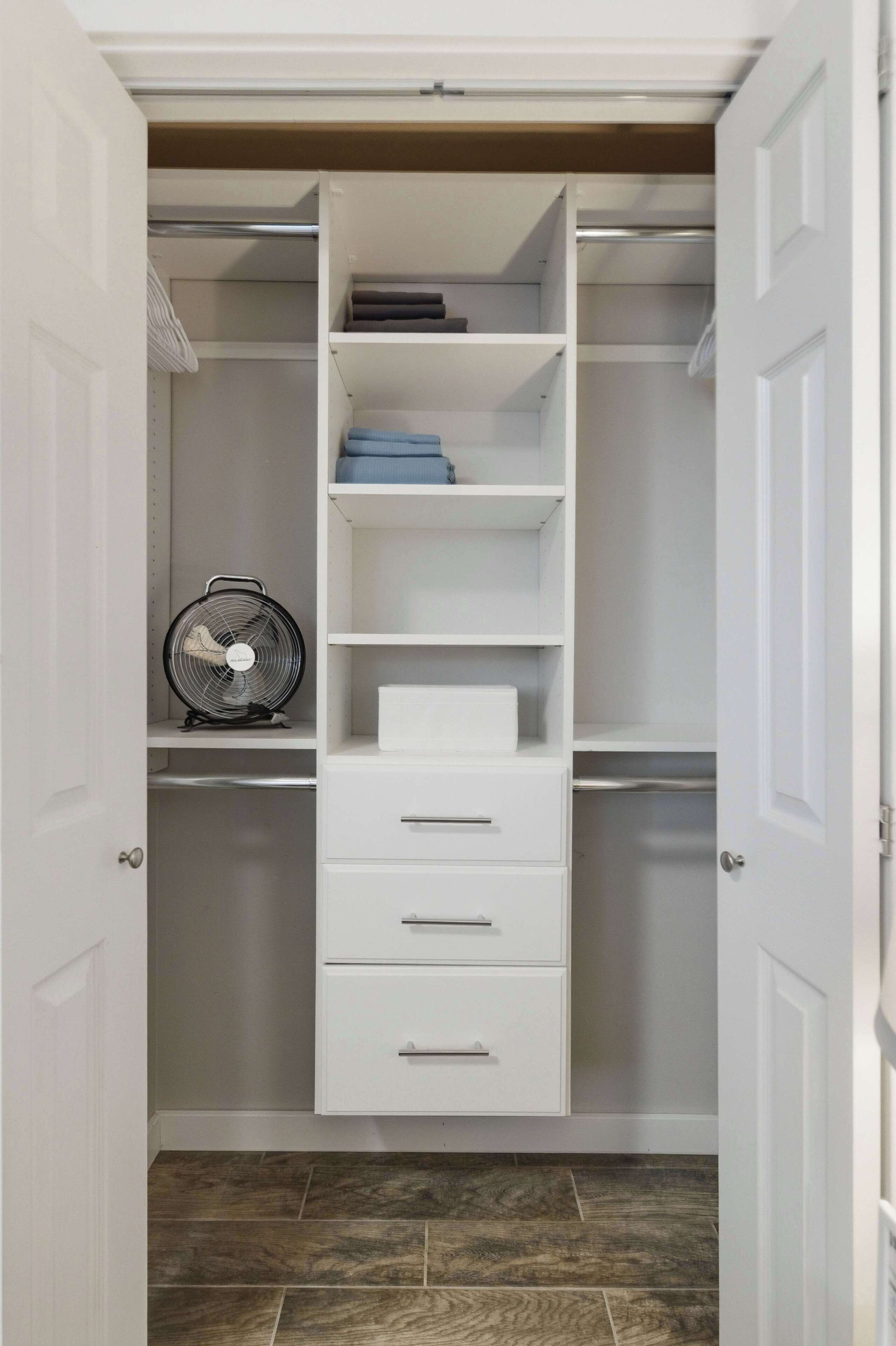 A walk-in closet with white shelving, a fan, and a tiled floor.