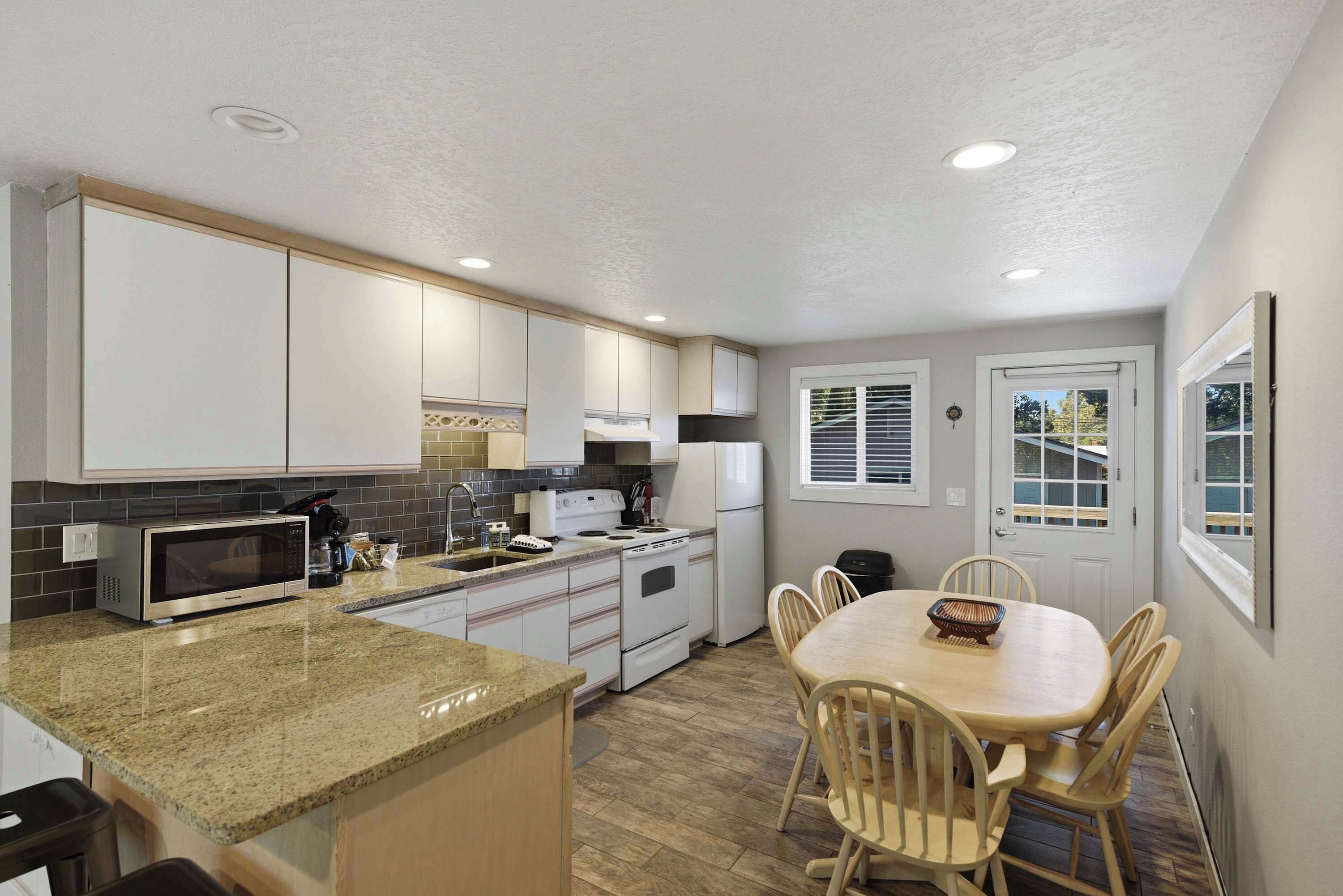 A compact kitchen with a granite countertop, white cabinets, a built-in microwave, and a dining area with a wooden table and chairs.