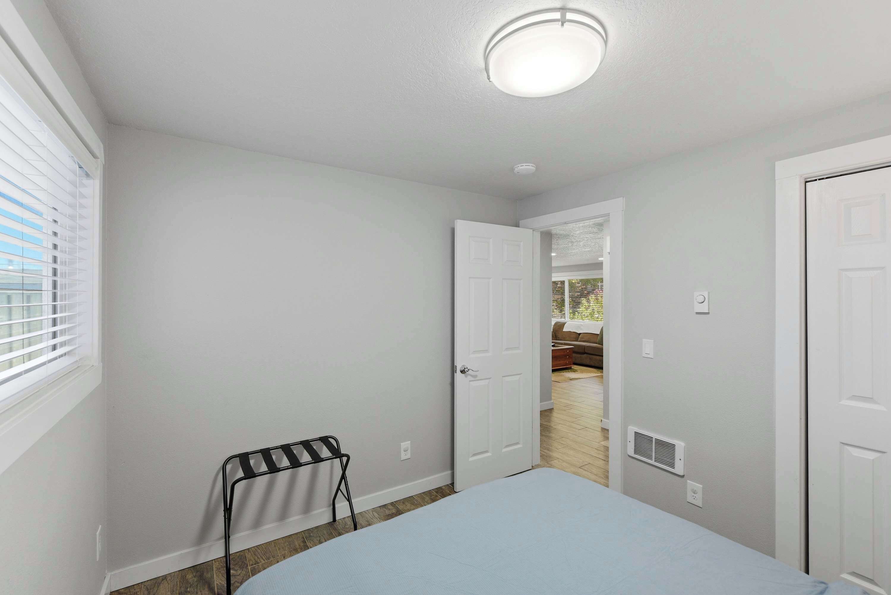 A bedroom with a bed, a radiator, a window with blinds, and a door leading to another room.