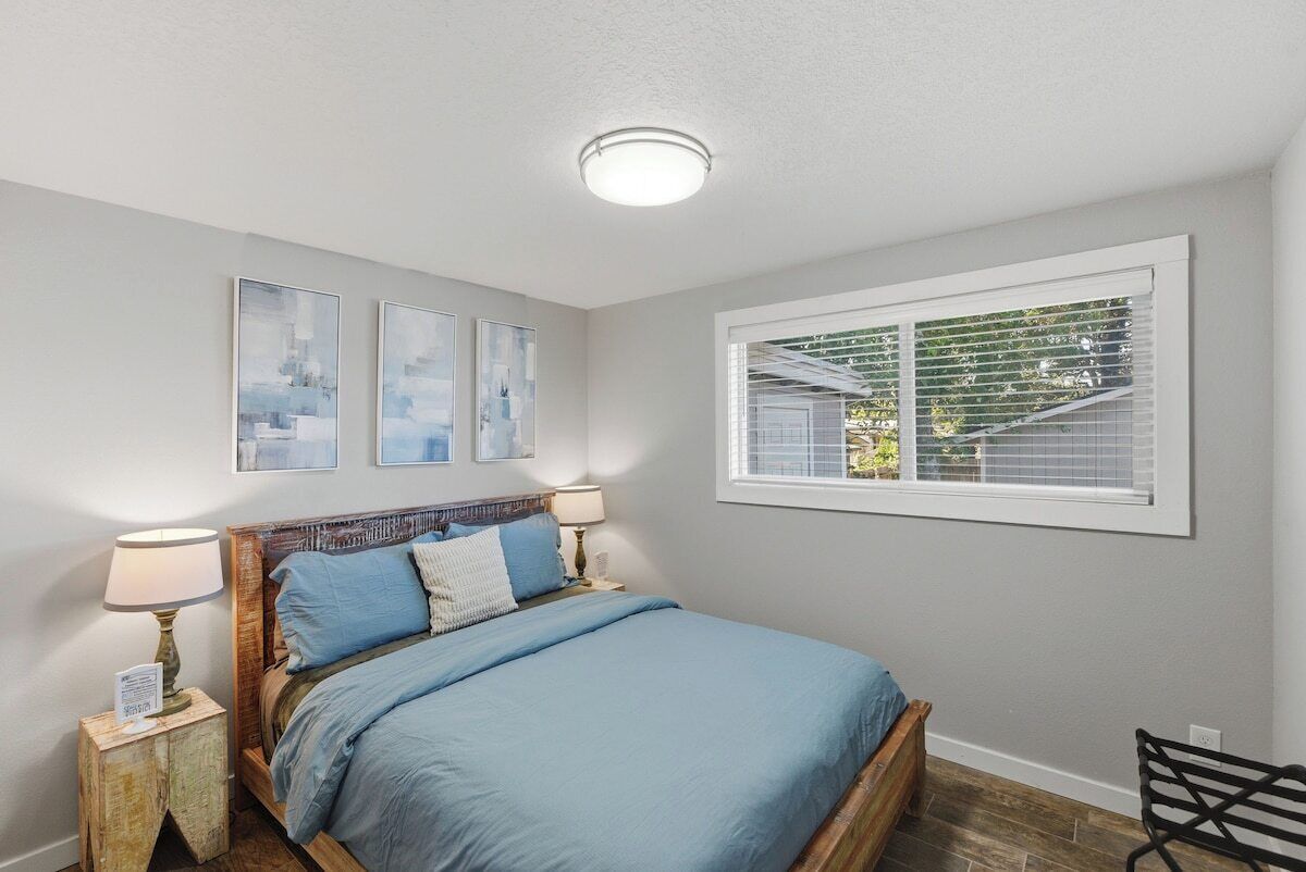 A bedroom with a bed, bedside tables, a window with blinds, and wall art.