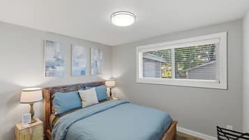 A bedroom with a bed, bedside tables, a window with blinds, and wall art.