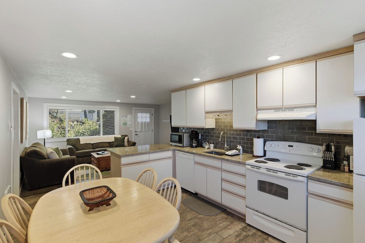 A compact kitchen with white cabinets, a stove, and a dining area with a table and chairs.