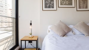 A bedroom with a bed, a bedside table with a lamp, and framed botanical prints on the wall. - Chic Modern Studio in Nunoa Vibran (Ñuñoa)