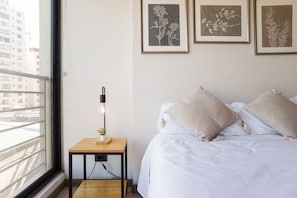 Ein Schlafzimmer mit einem Bett, einem Nachttisch mit Lampe und gerahmten botanischen Drucken an der Wand.