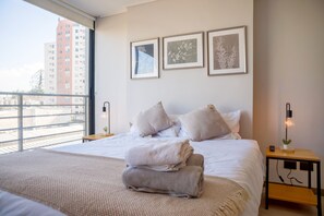 Ein Hotelzimmer mit einem großen Bett, Blick auf die Stadt und drei gerahmten Bildern an der Wand.
