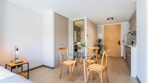 A modern hotel room with a glass dining table, wooden chairs, a small side table with a lamp, and a bed. - Chic Modern Studio in Nunoa Vibran (Ñuñoa)