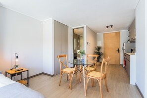 Ein modernes Hotelzimmer mit einem Glastisch, Holzstühlen, einem kleinen Beistelltisch mit Lampe und einem Bett.