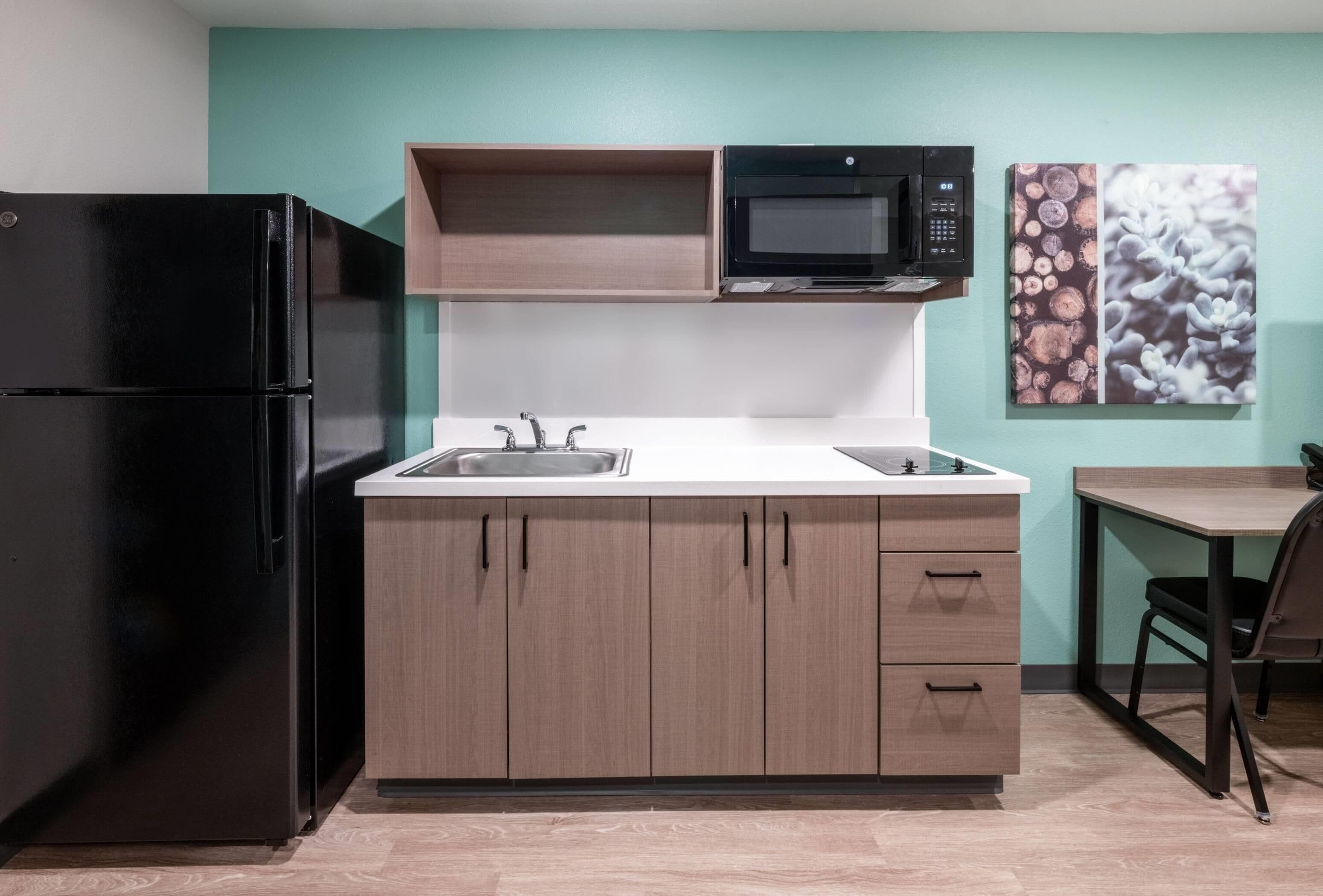 Cocina compacta con refrigerador negro, microondas, pileta y alacenas de madera.
