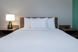 A hotel room with a large bed, white bedding, a bedside lamp, and a nightstand with a remote control. - Echo Suites Extended Stay By Wyndham Phoenix-Chandler (Chandler)