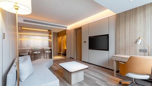 Una habitación de hotel moderna con sofá, escritorio, televisor y zona de comedor.