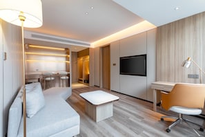 Una habitación de hotel moderna con sofá, escritorio, televisor y zona de comedor.
