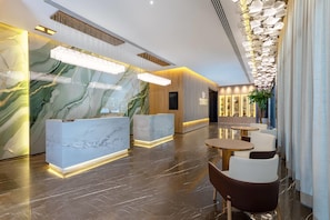 A modern hotel lobby with marble reception desks, a reception area, and seating arrangements.