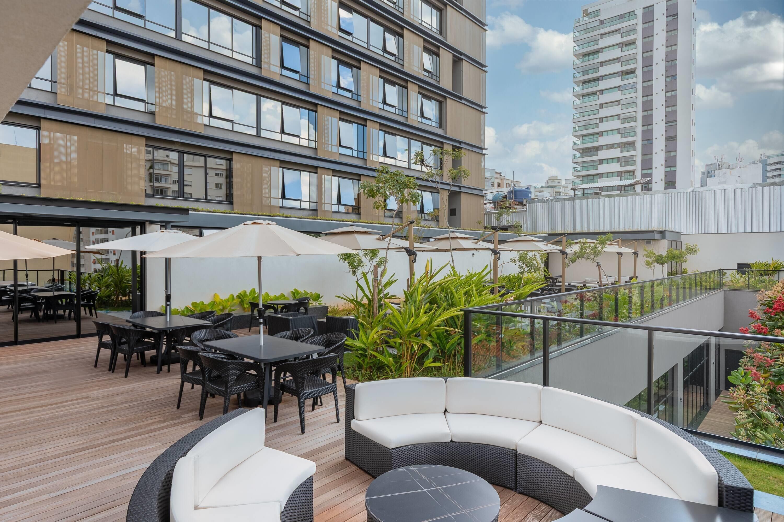 An outdoor seating area with tables and chairs, surrounded by greenery and overlooking a cityscape.