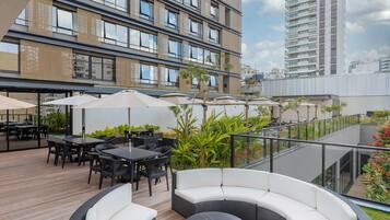 An outdoor seating area with tables and chairs, surrounded by greenery and overlooking a cityscape.