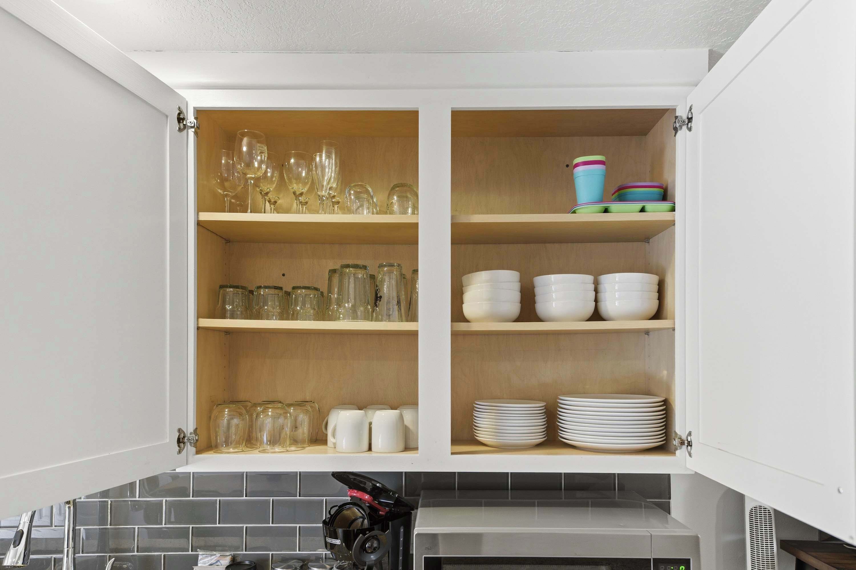 A kitchen cabinet with shelves containing glassware, mugs, and plates.