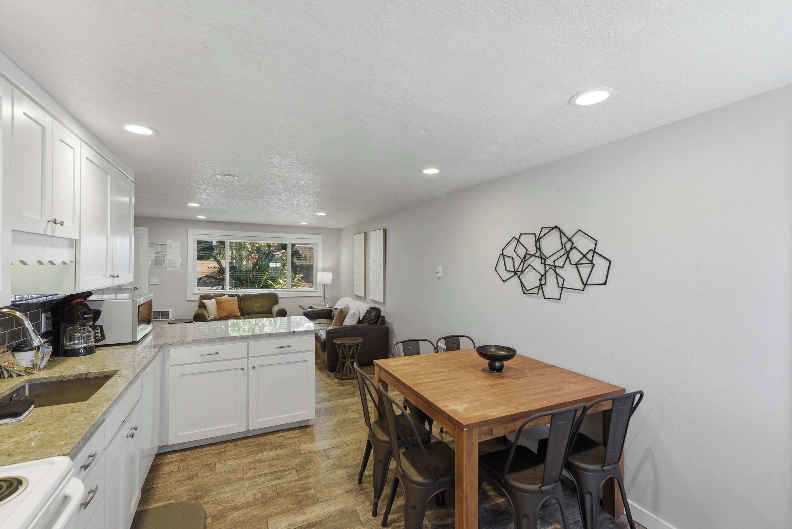 A modern kitchen with white cabinets, a dining area with a wooden table and chairs, and a decorative wall piece.