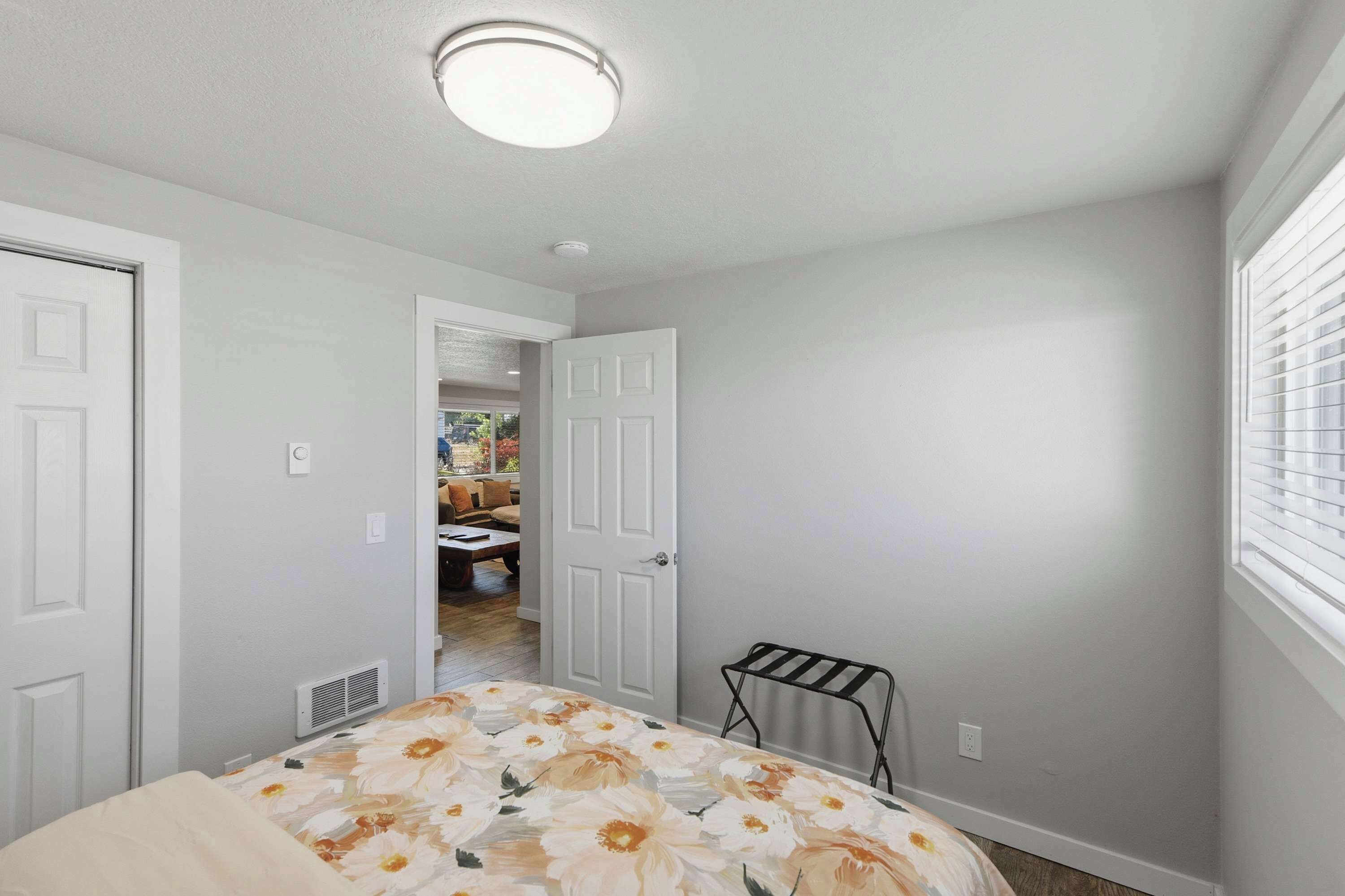 A bedroom with a bed, a radiator, a window with blinds, and a door leading to another room.