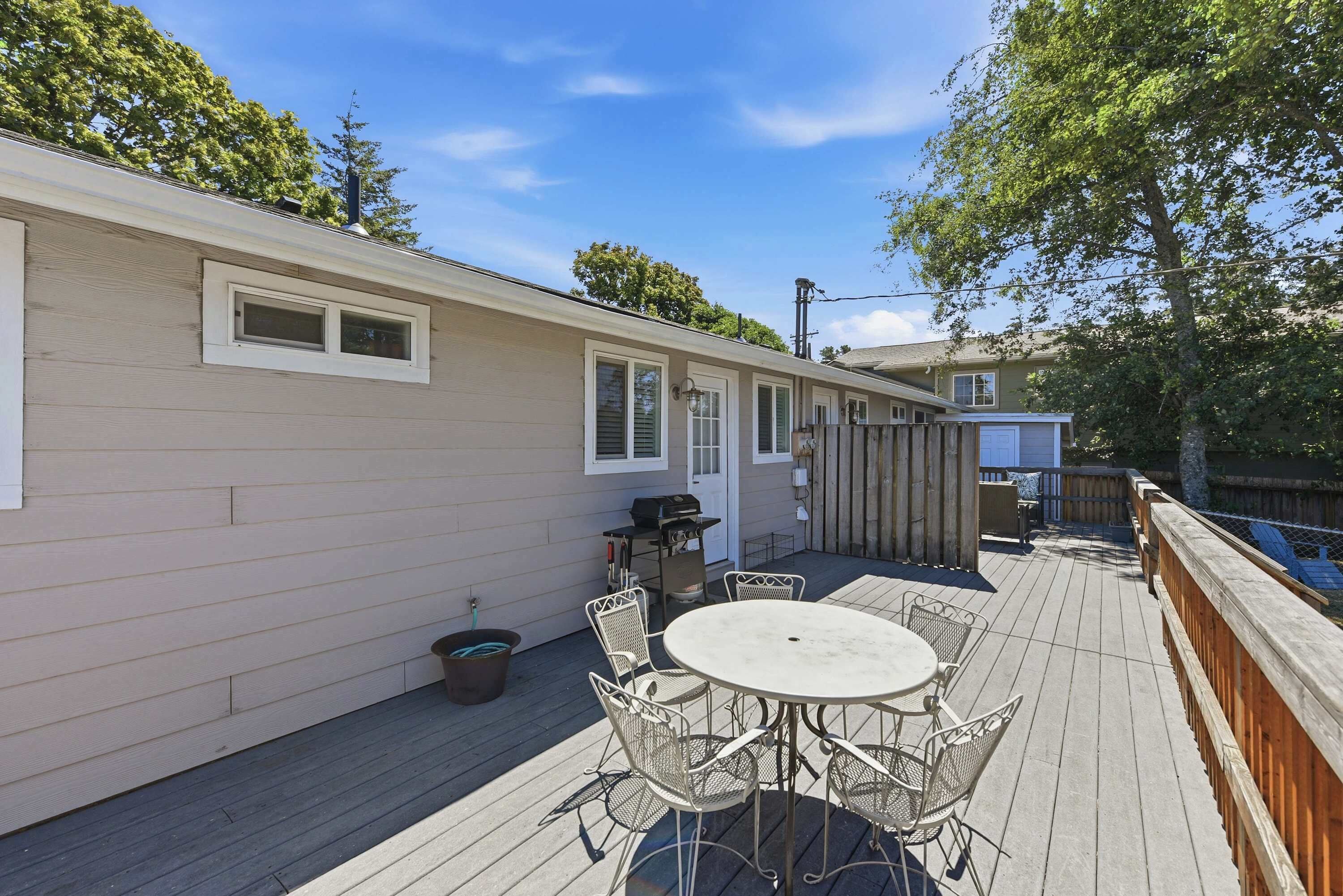 A covered patio with a round table and chairs, a grill, and a wooden deck.