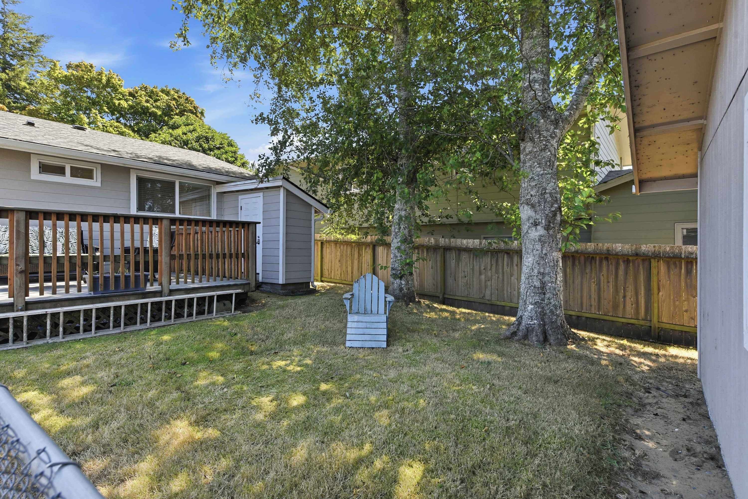 A backyard with a wooden deck, a shed, and a tree.