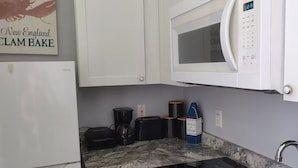Cocina compacta con armarios blancos, microondas integrado, cafetera y lavabo.
