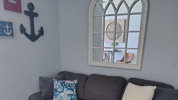 Una sala de estar con un sofá gris, una mesa de centro de madera con una planta y un ventanal decorativo con vista a un comedor.