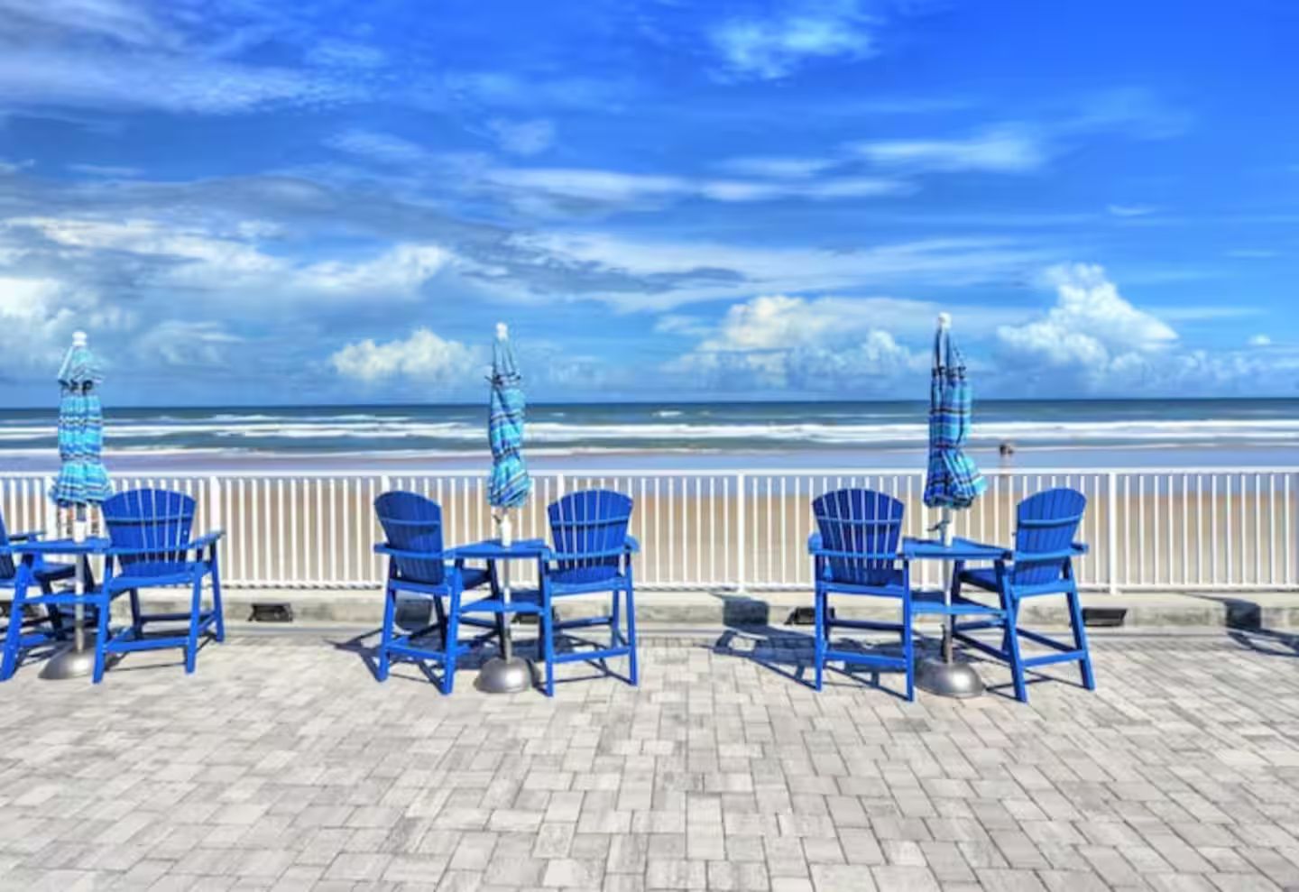 Un patio frente al mar con sillas y sombrillas azules, con vista al océano.