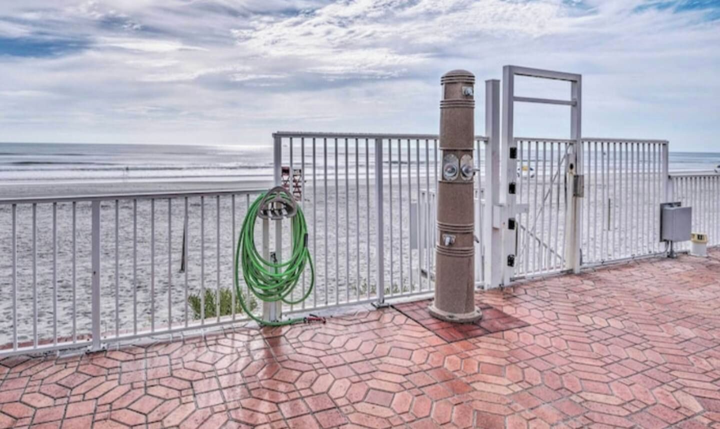A paved walkway with a metal railing, a green hose, and a gate with a clock.