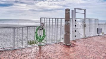 A paved walkway with a metal railing, a green hose, and a gate with a clock.