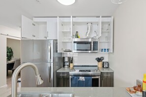 A modern kitchen with stainless steel appliances, white cabinetry, and a built-in microwave. - KING BED/ AC/ Henday /Whitemud (Edmonton)