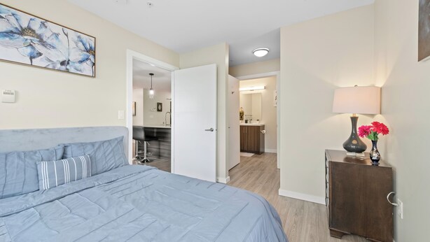 A bedroom with a bed, a bedside table with a lamp, and a painting on the wall.