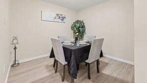 A dining area with a table set for four, surrounded by chairs, a plant, and a wall-mounted painting.