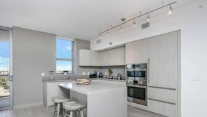 A modern kitchen with a central island, bar stools, built-in appliances, and a large window providing a view. - Cozy Apt - Corner Balcony w/360° Views (Hollywood)