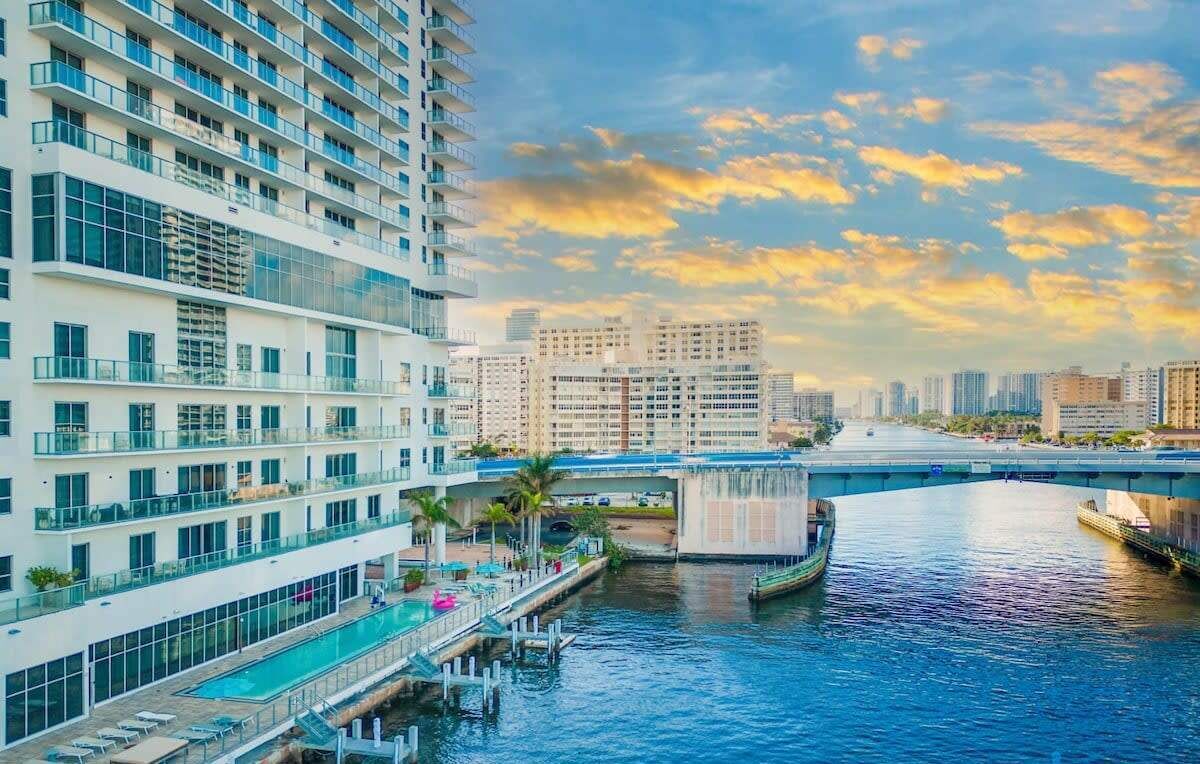 A modern hotel with a rooftop pool, a view of the waterway, and a cityscape in the background.