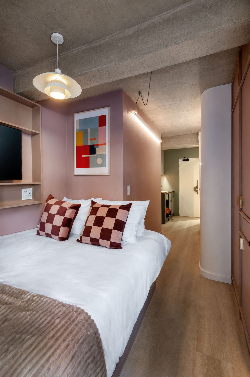 A modern bedroom with a bed, a wall-mounted TV, a ceiling light, and a hallway leading to a bathroom.