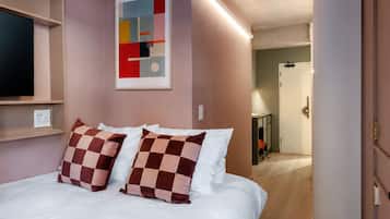Een moderne slaapkamer met een bed, een tv aan de muur, een plafondlamp en een gang naar een badkamer.