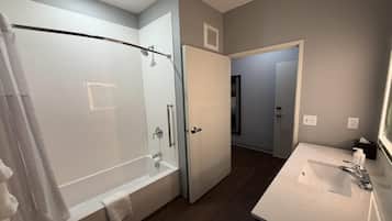 A modern bathroom with a glass-enclosed shower, a white sink, and a door leading to another room.