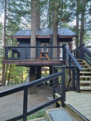 A treehouse with a wooden deck, a metal staircase, and a small window.