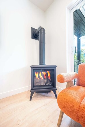 A modern room with a wood-burning stove, a wooden floor, and a large window.