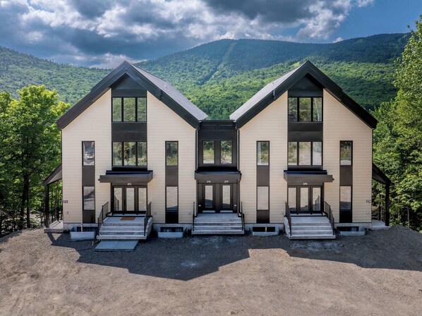 A modern two-story building with large windows and a symmetrical design, set against a backdrop of lush green hills.