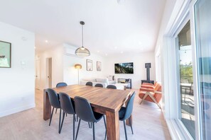 A modern dining area with a wooden table and chairs, a pendant light, and a sofa with orange cushions.