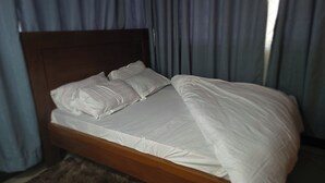 Een bed met een houten hoofdbord, witte beddengoed en een bruin vloerkleed.