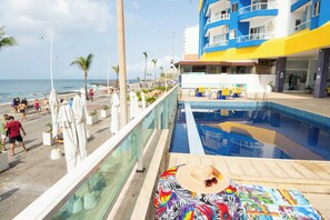 Ein Poolbereich mit Blick auf den Ozean, ein Gebäude mit Balkonen und ein Strandpromenade.