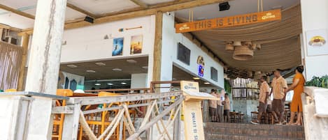 A restaurant with a wooden entrance, outdoor seating, and a sign that reads 'THIS IS LIVING'.