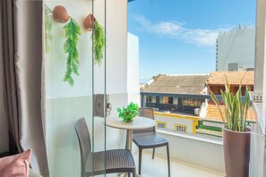 Un balcon avec une porte-fenêtre, deux chaises, une petite table et des plantes en pot.
