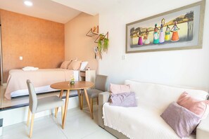 A hotel room with a bed, a sofa, a dining table, and a painting on the wall. - Beachfront Living: Pool & Beach in Barra (Salvador)